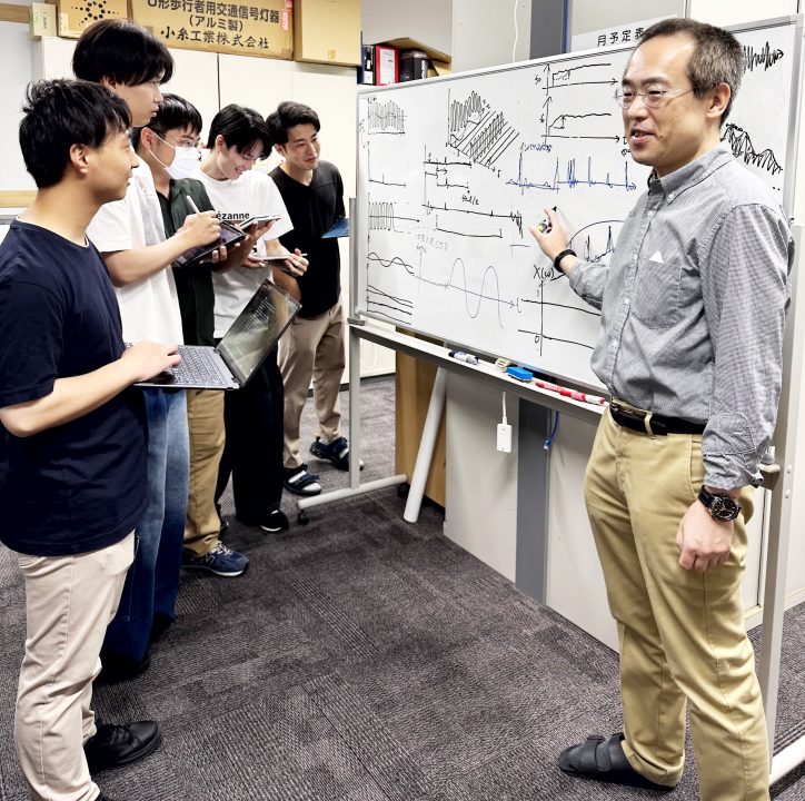 指導風景(教員居室)。教員室のホワイトボードを使って学生に説明する坂野先生