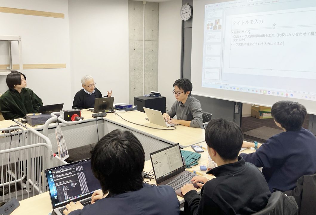 研究室のゼミで学生の発表にコメントする山田先生